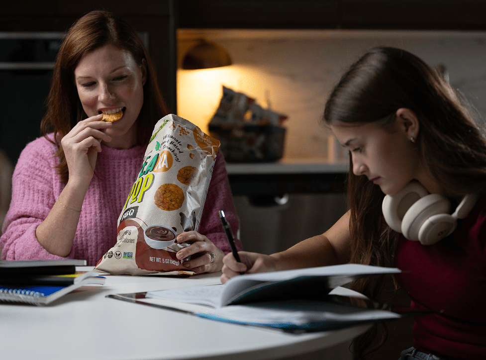 Two women at a table with one eating PeaKaPop and the other studying.
