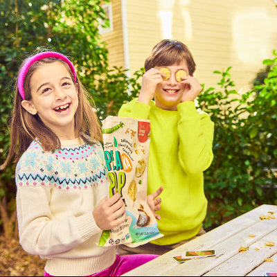 Two children outdoors with a box of snacks, smiling and having fun.
